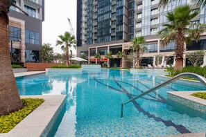 A modern hotel with a swimming pool, palm trees, and a view of high-rise buildings.