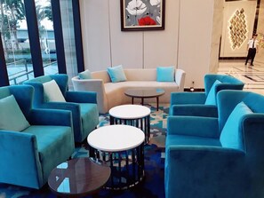 A modern lounge area with blue sofas, round tables, and a large window offering a view of the outdoors.