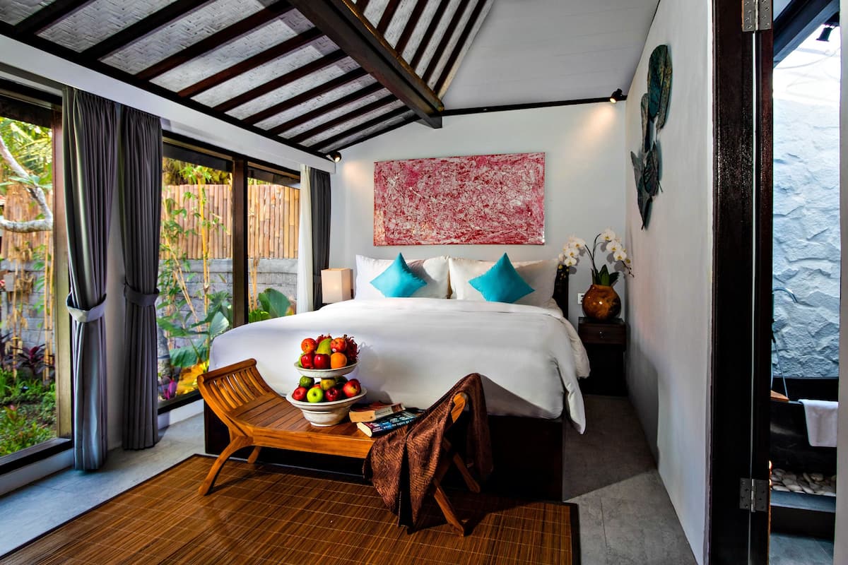Un dormitorio moderno con una cama grande, una silla de madera, un frutero y vistas a zonas verdes al exterior.