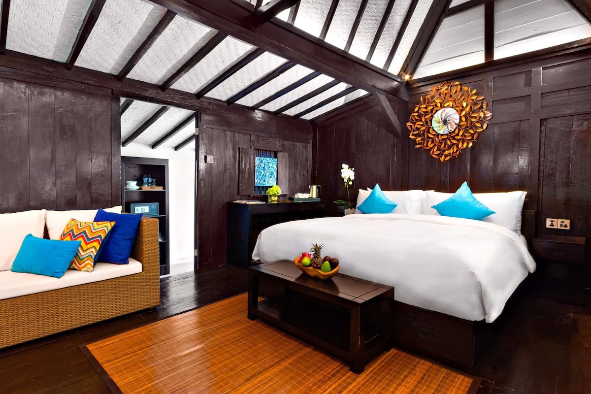 Una habitación con cama, sofá, suelo de madera, techo con vigas de madera y pared con un diseño circular decorativo.
