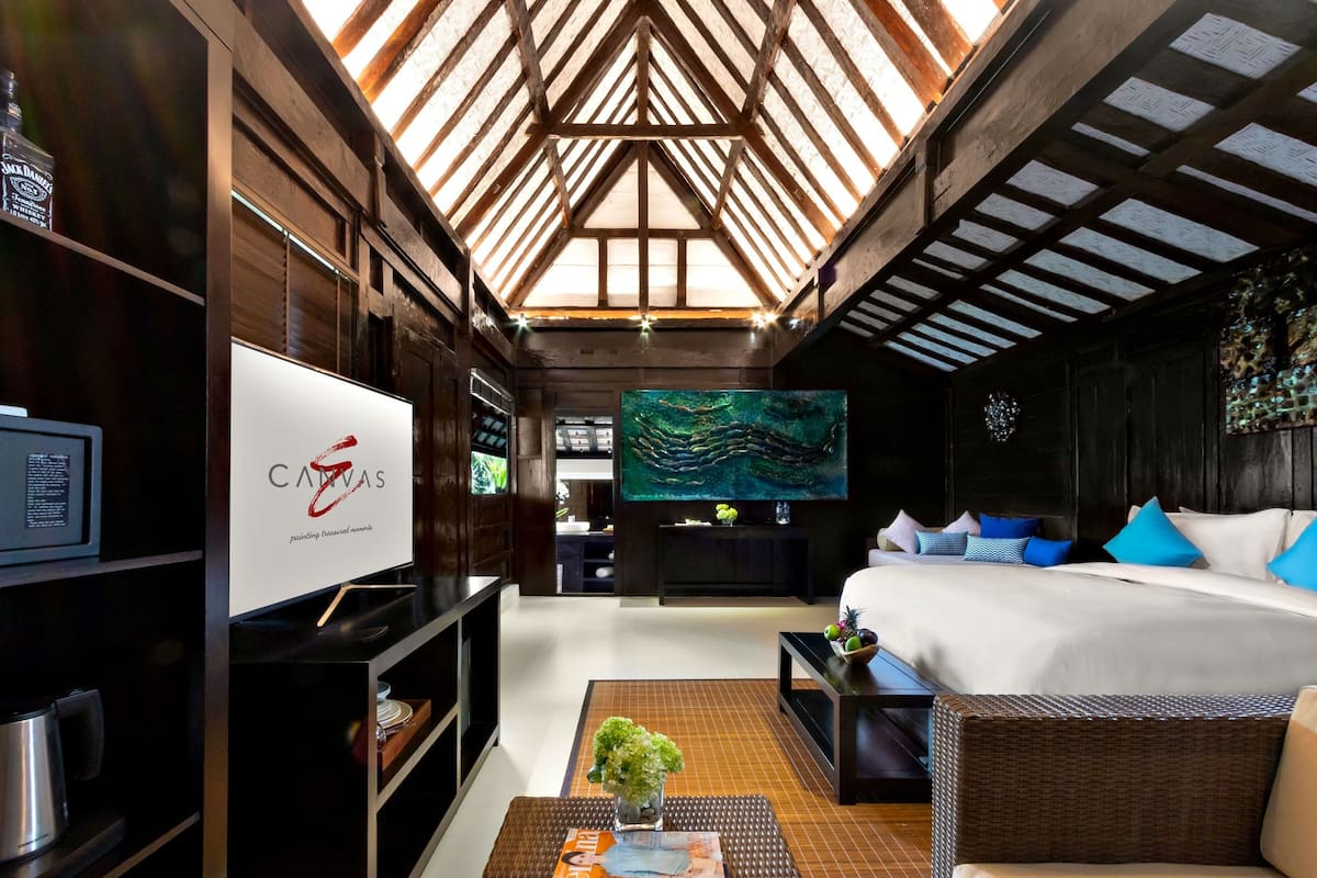 Una habitación de hotel moderna con techo alto, un cuadro grande, una cama con ropa de cama azul y blanca, un televisor y una cafetera.