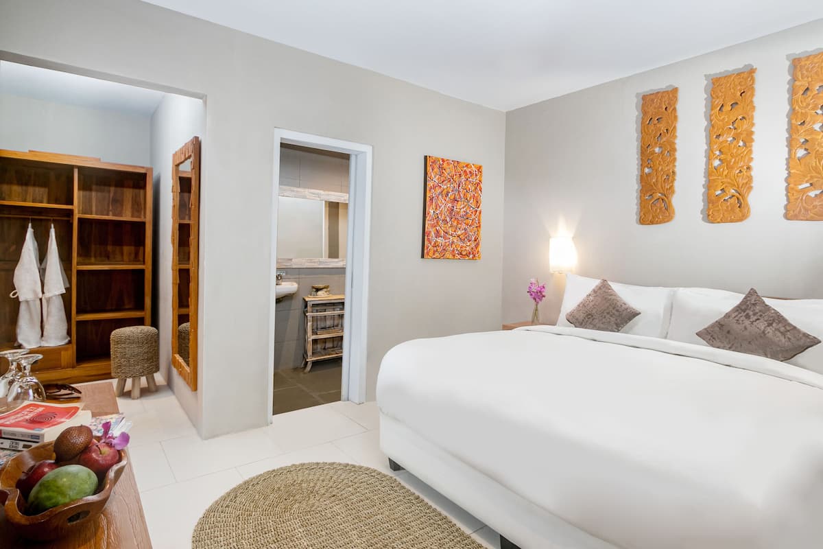 Un dormitorio con una cama grande, un armario de madera, un taburete pequeño y un estante en la pared.