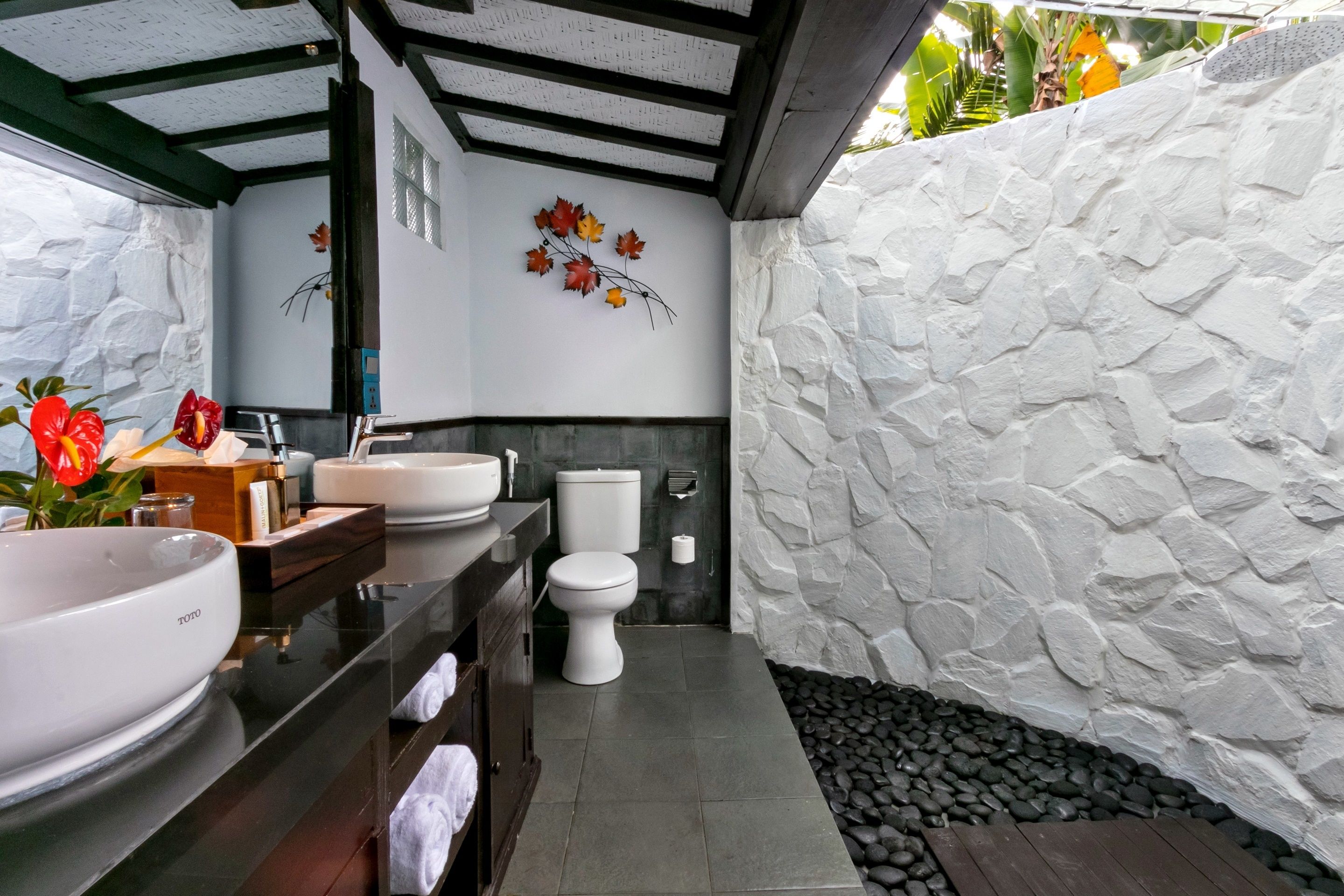 A modern bathroom with a stone wall, a white sink, and a toilet.