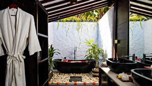 Un baño moderno con una bañera grande, dos lavamanos negros y una bata colgada en un perchero.