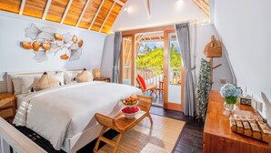 Un dormitorio amplio con una cama grande, techo de madera y un balcón con vistas a zonas verdes.