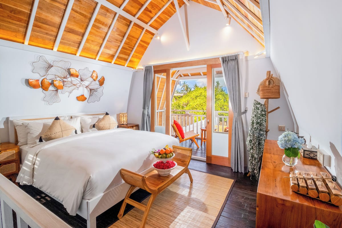 Un dormitorio amplio con una cama grande, techo de madera y un balcón con vistas a zonas verdes.