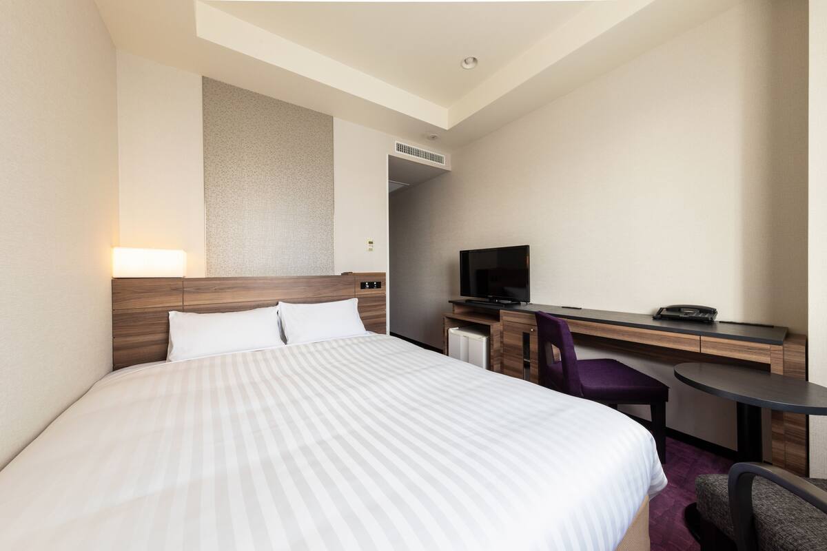 A hotel room with a large bed, a desk with a chair, a television, and a small table.