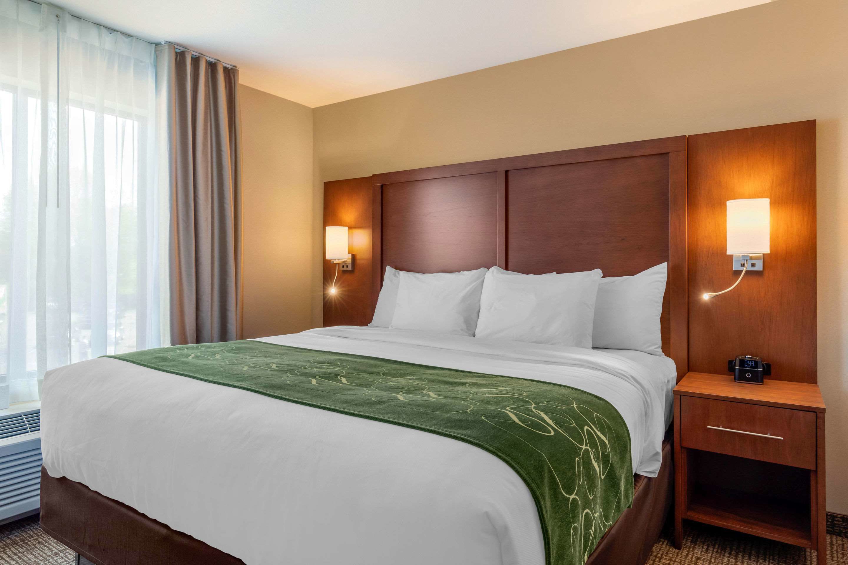 Habitación de hotel con una cama grande, dos lámparas de noche, una mesita de noche y un ventanal con cortinas.