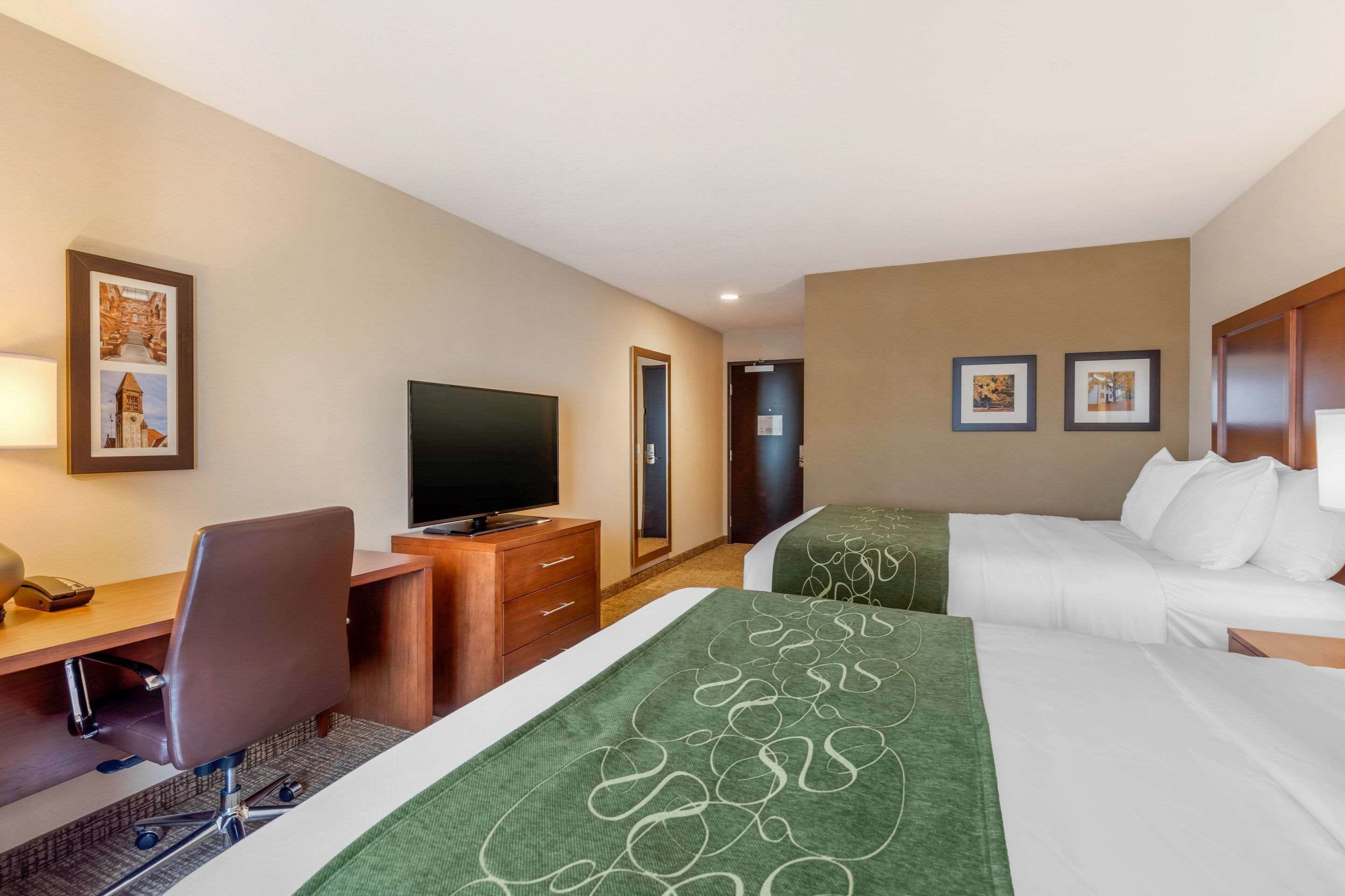 A hotel room with a desk, a TV, two beds, and framed pictures on the walls.