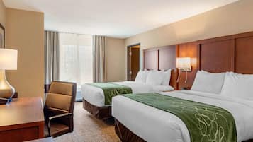 Une chambre d’hôtel avec deux lits, un bureau, une chaise et une fenêtre avec des rideaux.
