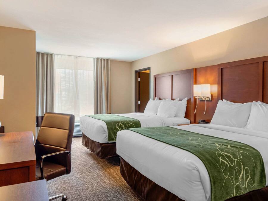 Une chambre d’hôtel avec deux lits, un bureau, une chaise et une fenêtre avec des rideaux.
