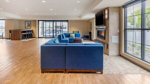 A spacious lobby with a large blue sectional sofa, a flat-screen TV mounted on the wall, and a fireplace.