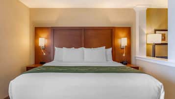 A hotel room with a large bed, two bedside tables, a nightstand, a window with a view, and wall-mounted lamps.