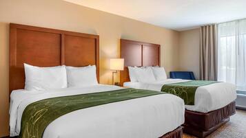 A hotel room with two beds, a nightstand, a lamp, and a view of the outdoors.