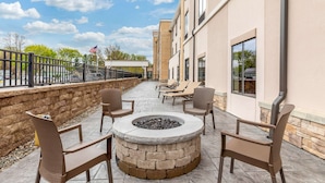An outdoor patio with a stone fire pit, lounge chairs, and a stone wall.