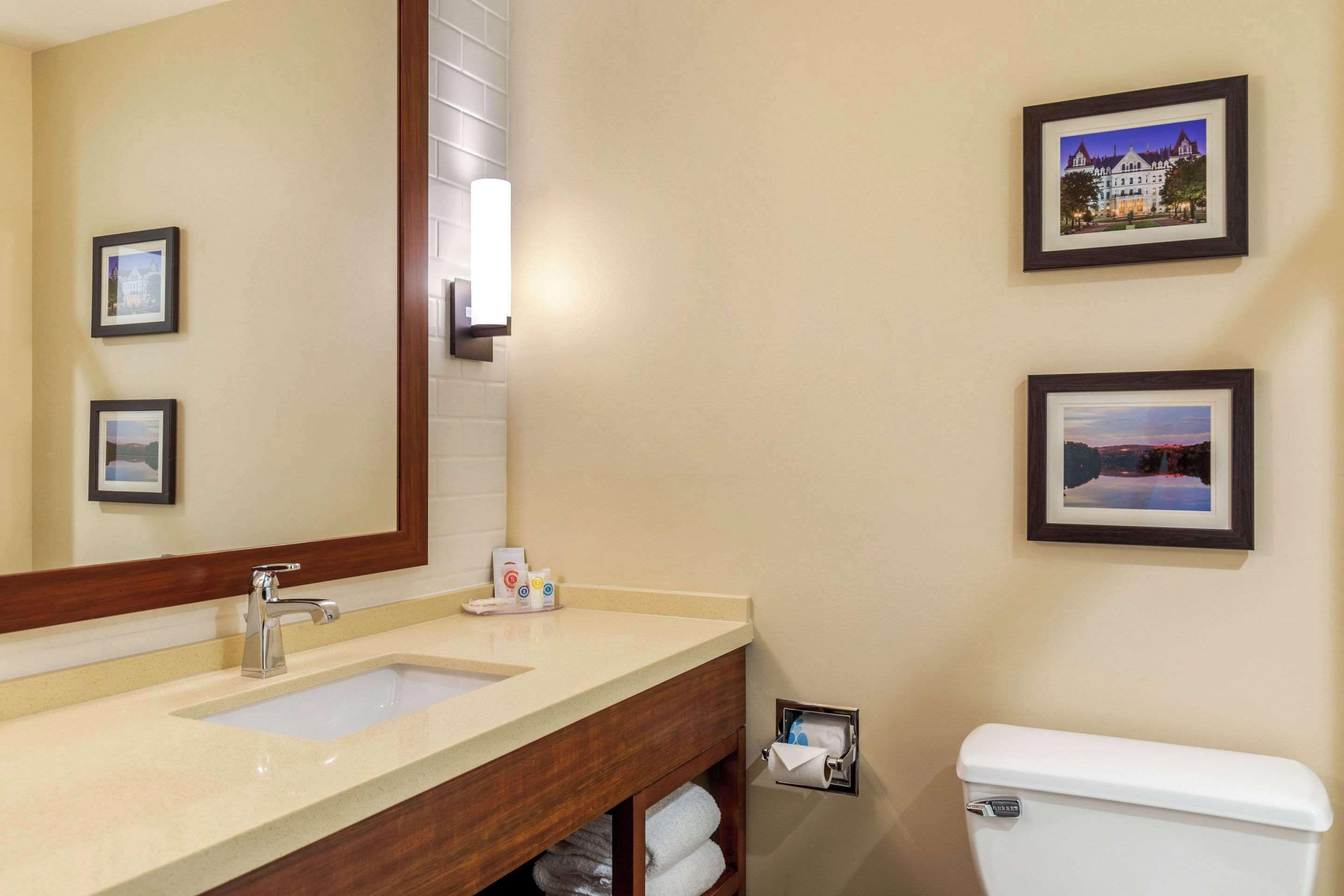 Une salle de bain avec un double lavabo, des toilettes et des tableaux encadrés au mur.