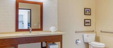A bathroom with a white sink, mirror, and toilet. There are towels on a shelf, and a picture frame on the wall.