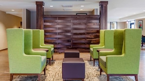 A lobby with green upholstered chairs, a patterned rug, and a wooden wall with a horizontal design.