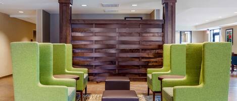 A lobby with green upholstered chairs, a patterned rug, and a wooden wall with a horizontal design.