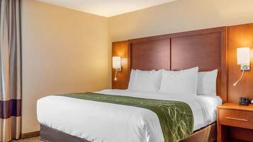 A hotel room with a large bed, wooden headboard, bedside lamps, and a nightstand.