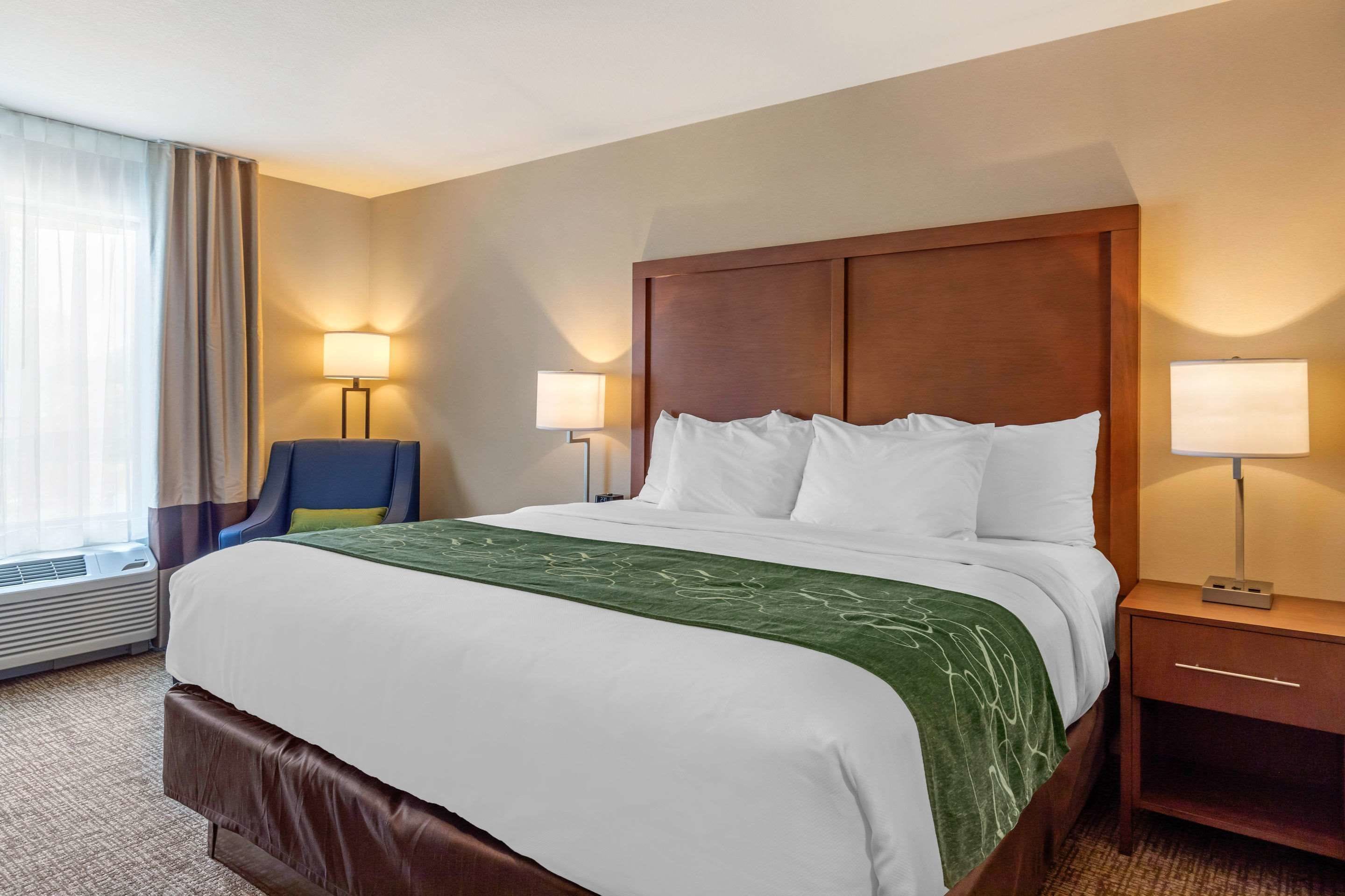 A hotel room with a large bed, two bedside tables with lamps, a chair, and a window with curtains.