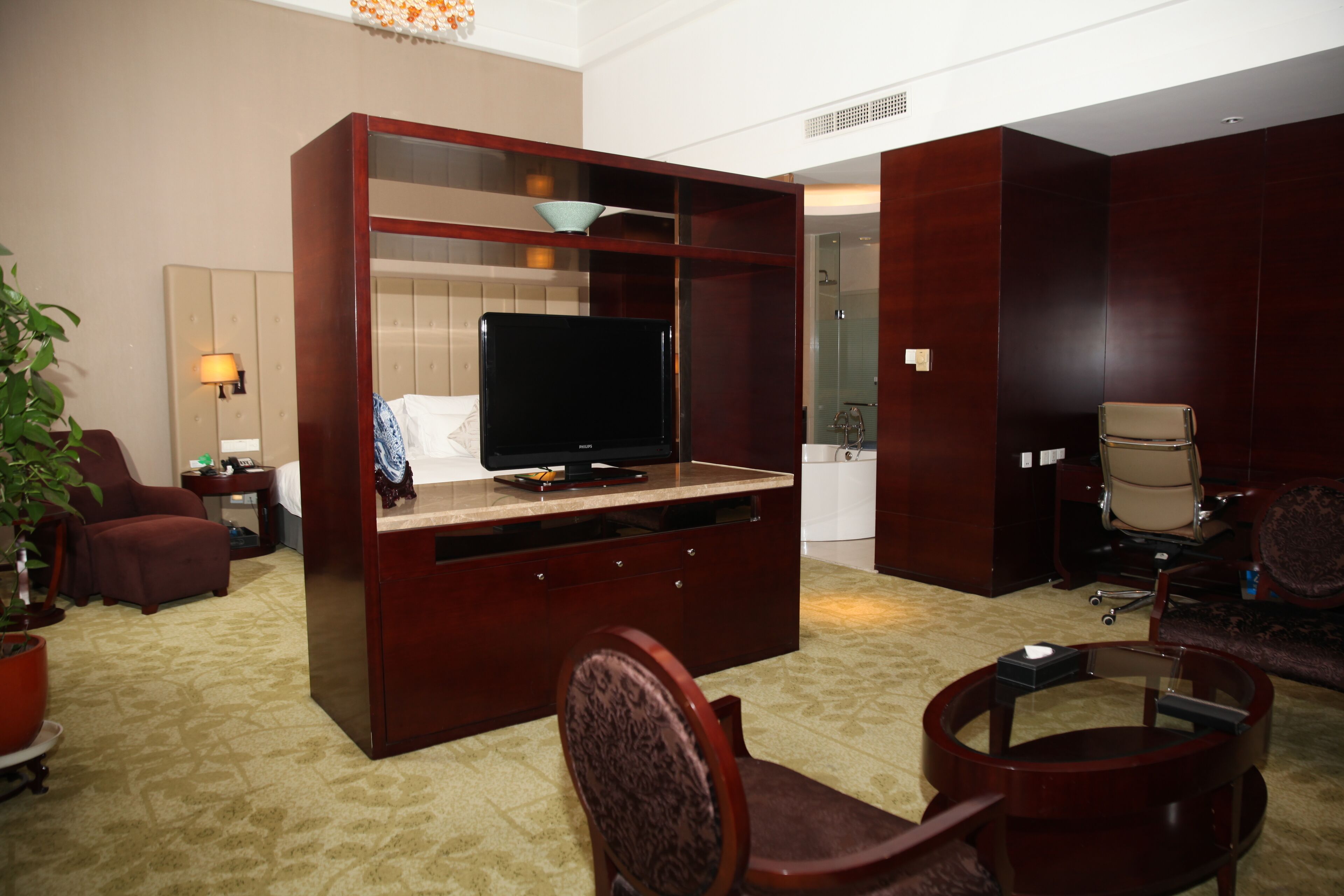 Una habitación de hotel con un escritorio grande de madera, un televisor, un sofá y una silla.
