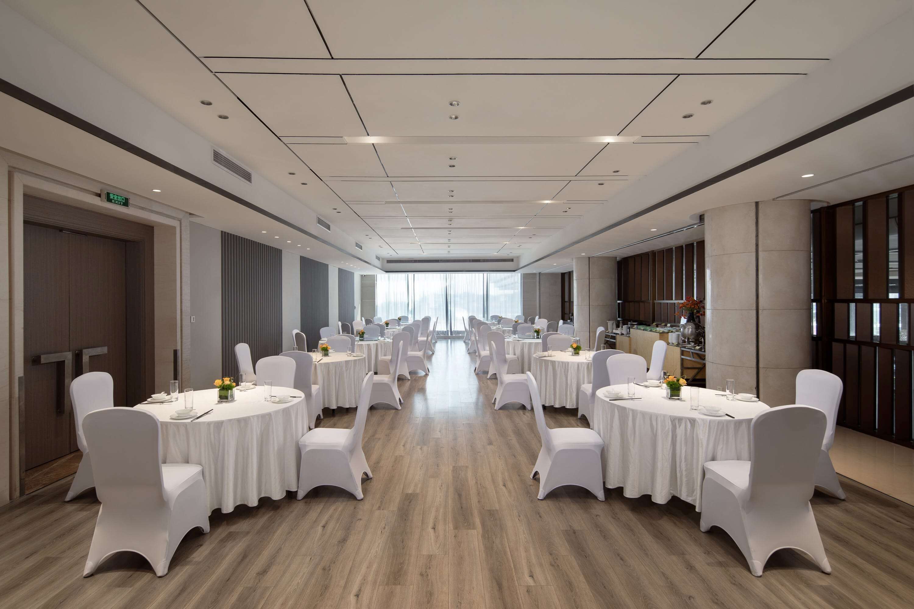 A conference room with round tables, white chairs, and a wooden floor.