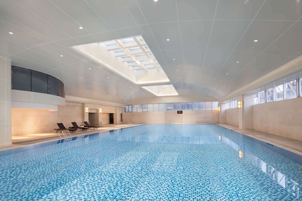 Una piscina interior con tragaluces, sillas de descanso y vistas despejadas al cielo.