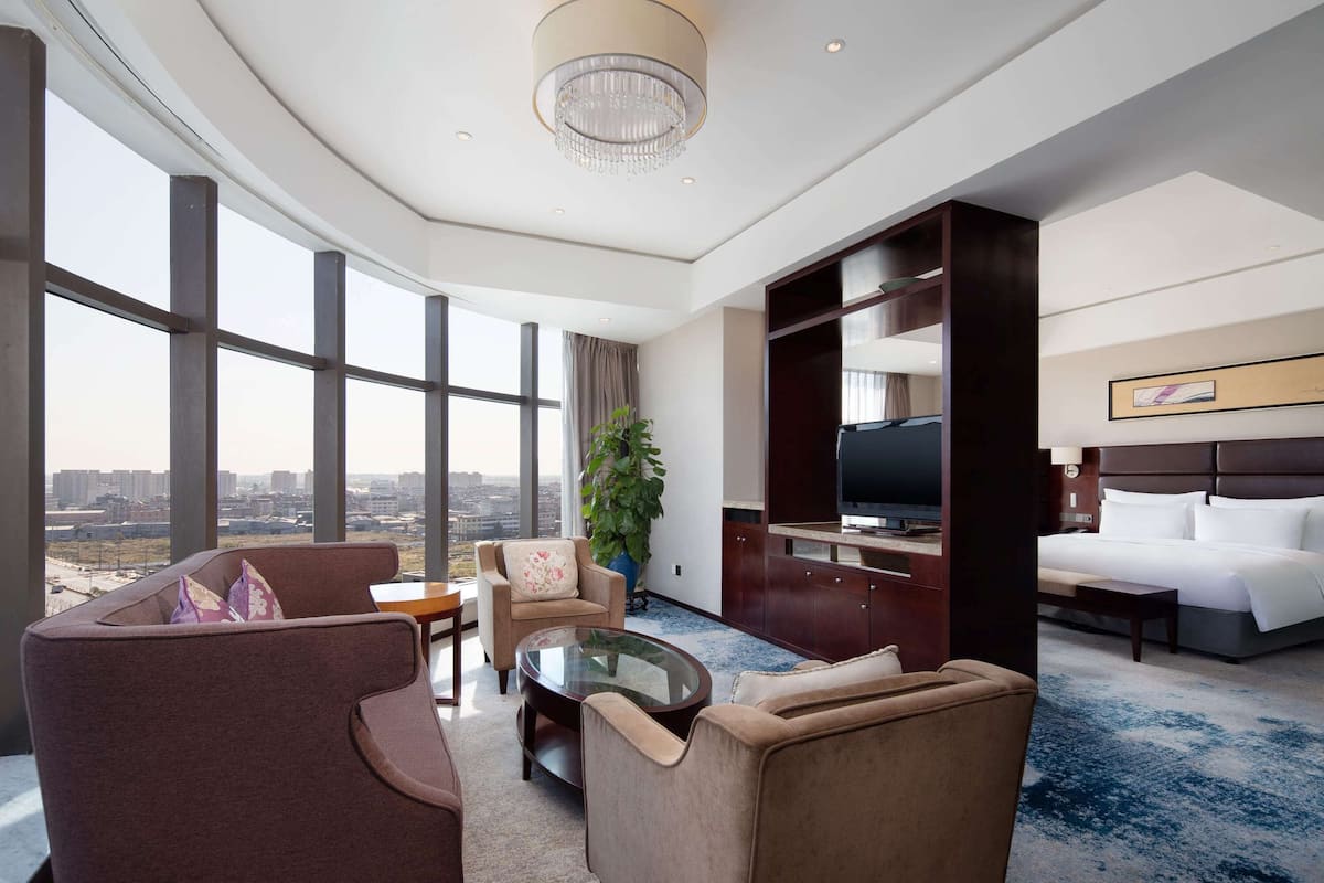 A hotel room with a large window, a television, a bed, and a seating area with a coffee table.