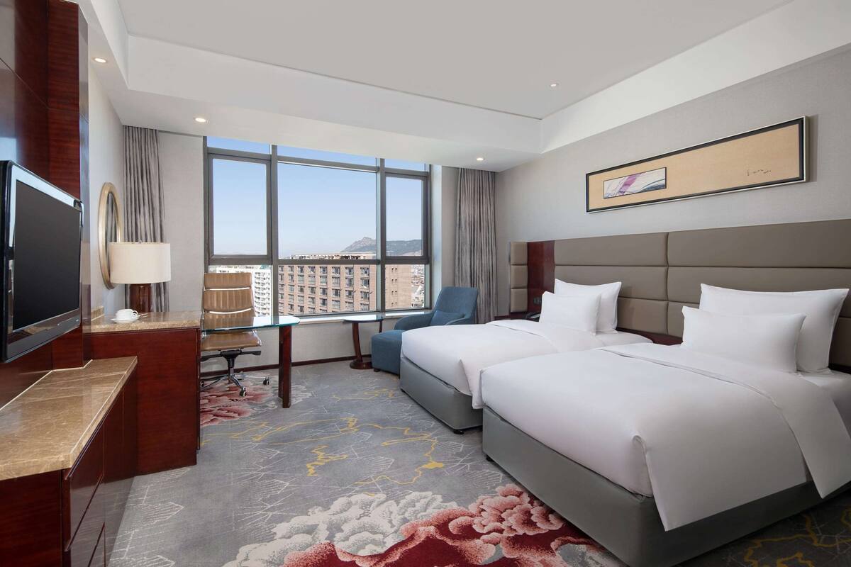 A hotel room with a large bed, a desk, a chair, and a TV.
