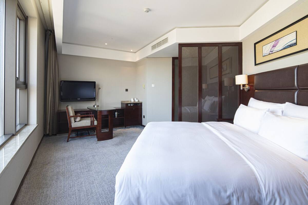 A hotel room with a large bed, a desk with a chair, a television, and a sliding door closet.