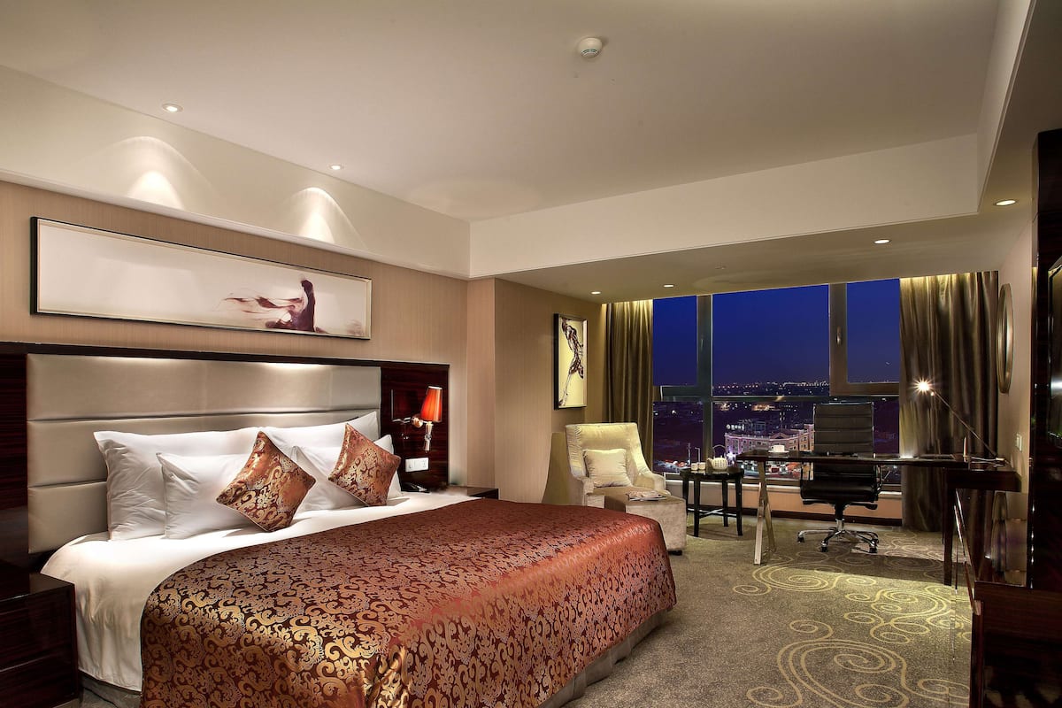 A hotel room with a large bed, a desk, and a view of the city at night.