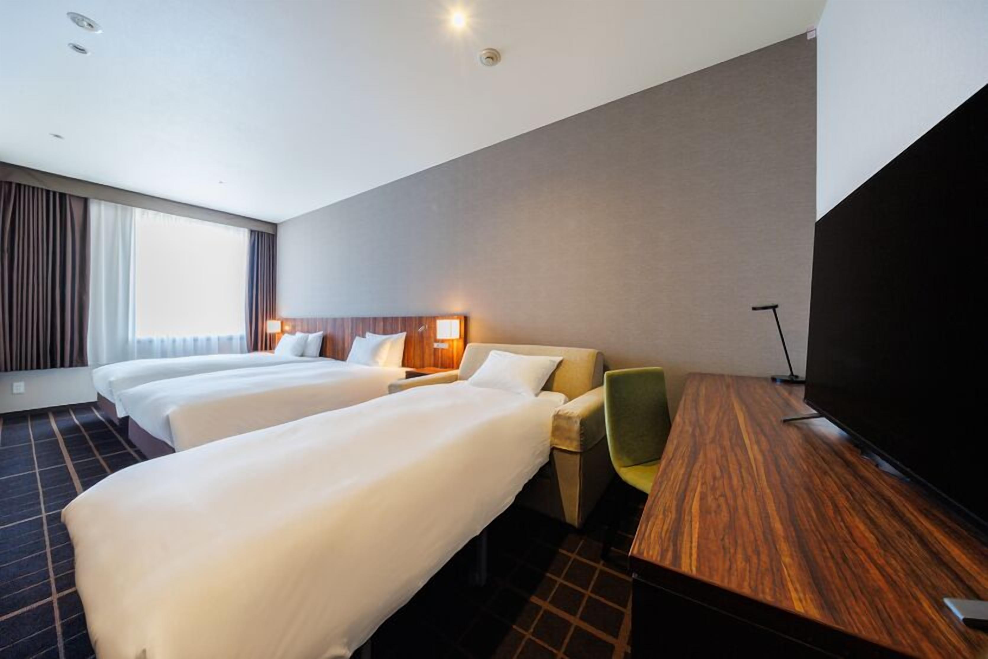 Une chambre d’hôtel avec deux lits, un bureau, une chaise, un téléviseur à écran plat et une grande fenêtre.