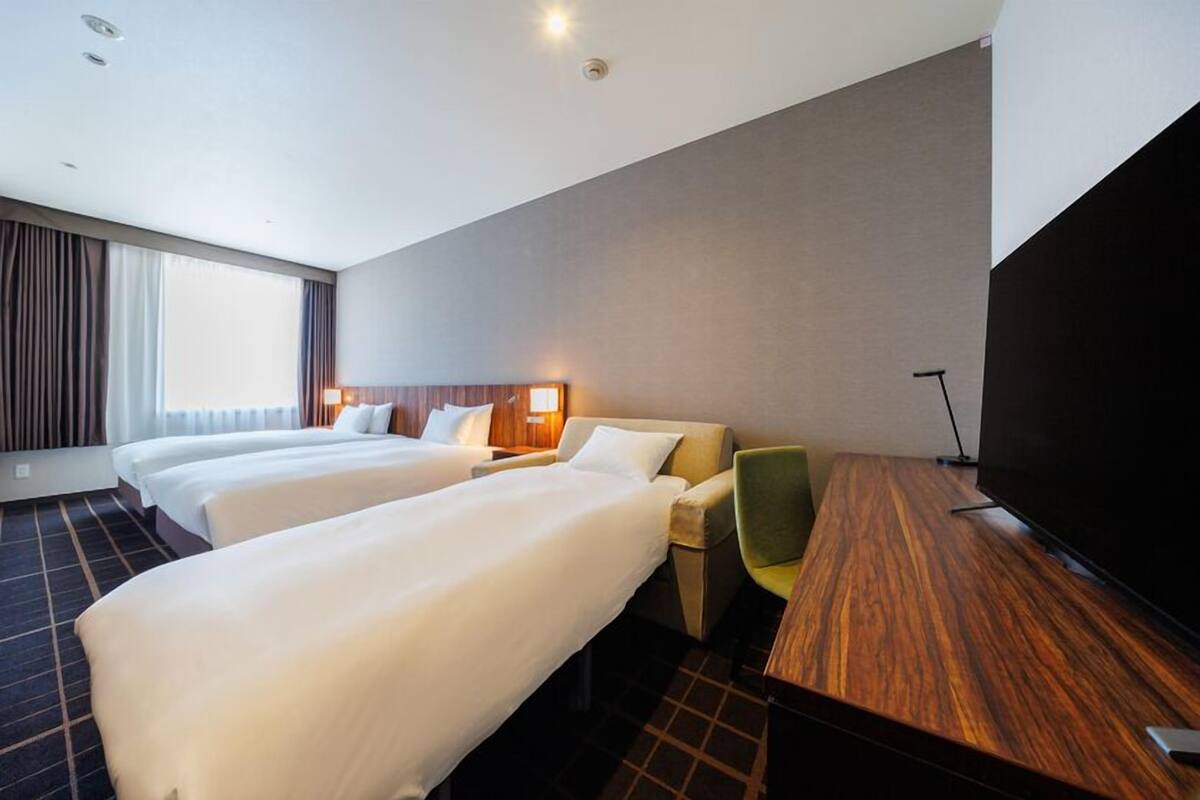 Een hotelkamer met twee bedden, een bureau, een stoel, een flatscreen televisie en een groot raam.