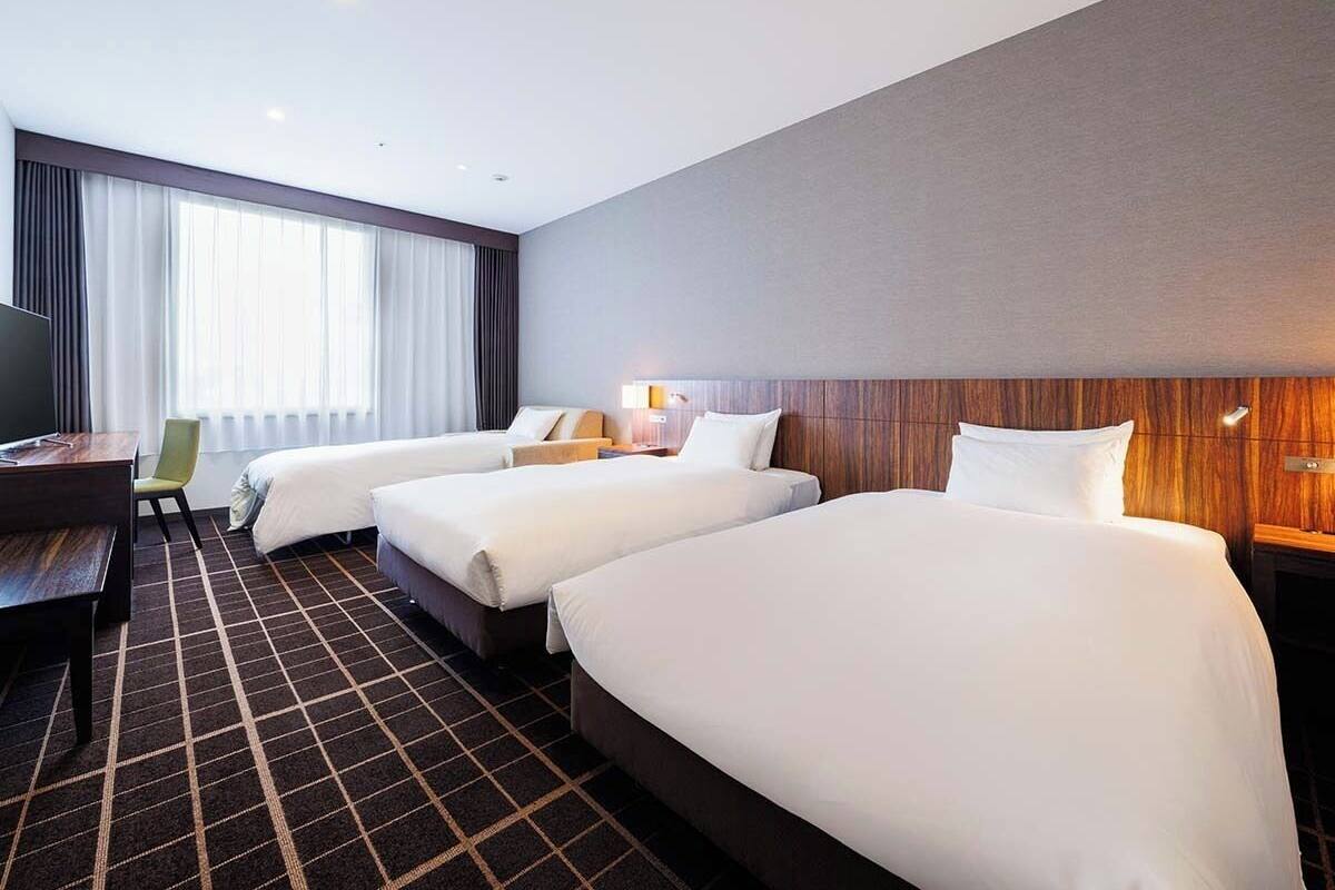 Een hotelkamer met drie bedden, een bureau, een stoel en een televisie.