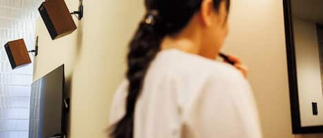 A person in a white shirt in a room with a flat-screen TV mounted on the wall, a mirror, and a wooden object on the wall.