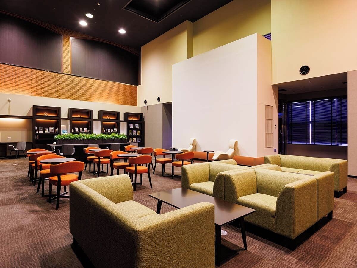A hotel lobby with seating areas, a reception desk, and a large window with blinds.