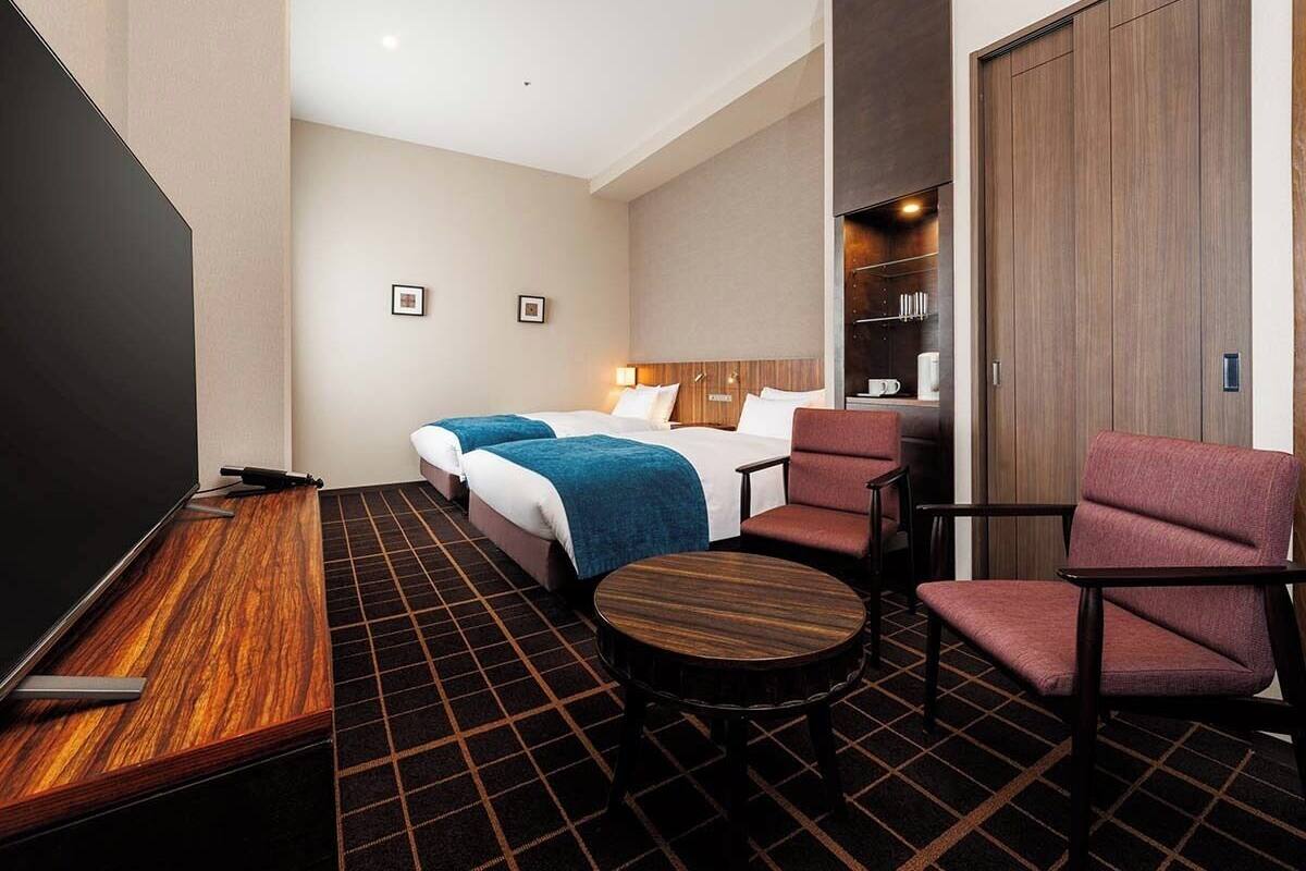 Een hotelkamer met een bed, twee nachtkastjes, een televisie, een zithoek met een tafel en stoelen, en een kledingkast.