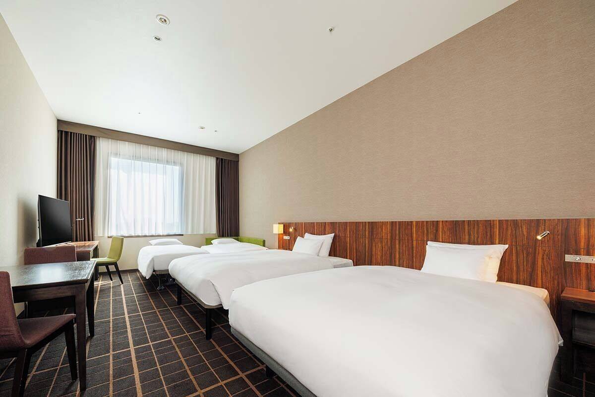 Een hotelkamer met twee bedden, een bureau, een televisie en een groot raam met gordijnen.