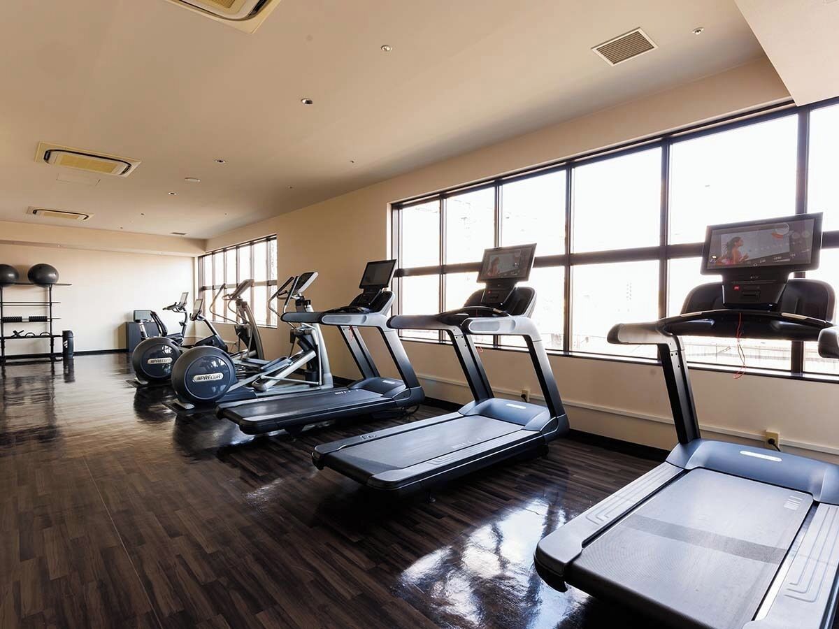A gym with treadmills, elliptical machines, and a TV screen.