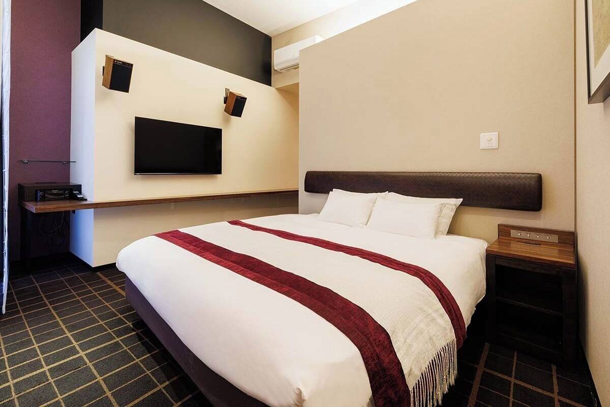 Een hotelkamer met een bed, een wandgemonteerde flatscreen televisie, een nachtkastje en een stopcontact.