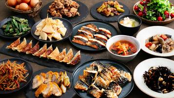 Une variété de plats, notamment du poisson grillé, des légumes et une salade, sont disposés sur une table.