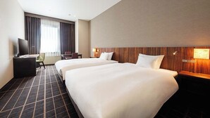 A hotel room with two beds, a desk, a chair, a TV, and a large window with curtains.