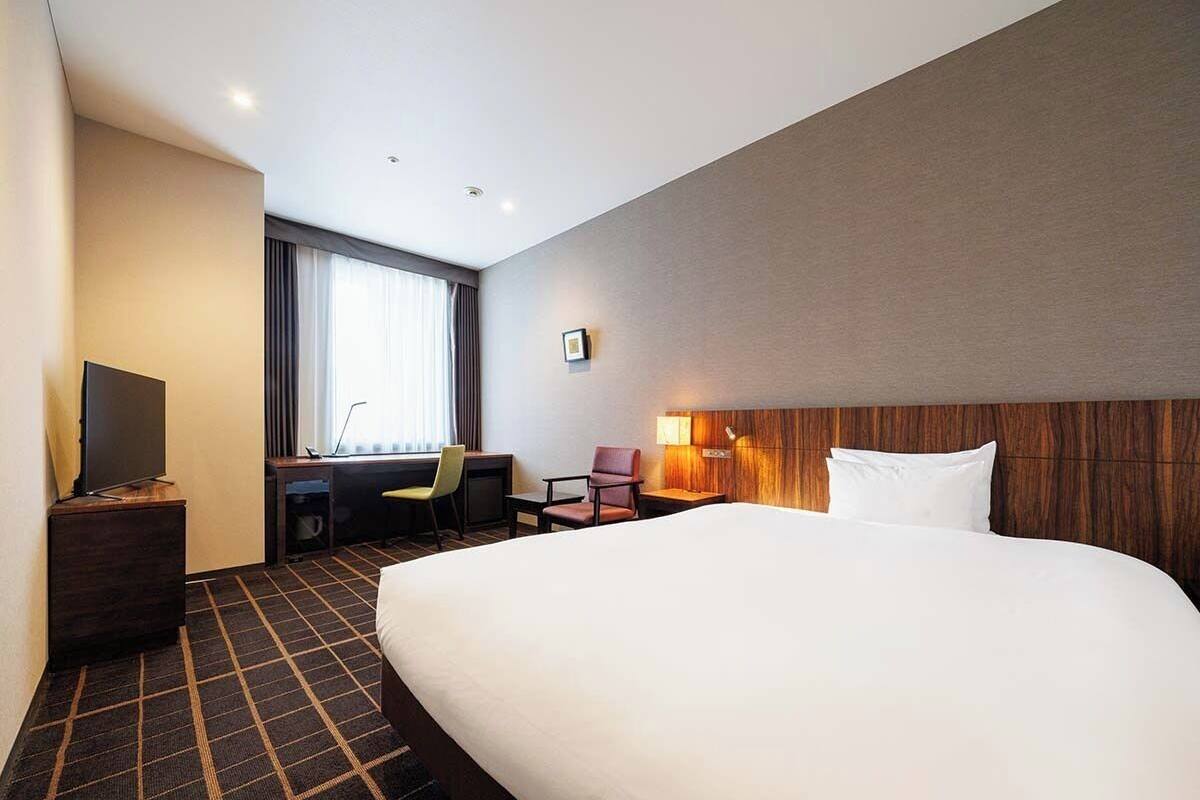 Een hotelkamer met een groot bed, een bureau met stoel, een televisie en een raam met gordijnen.