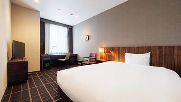 A hotel room with a large bed, a desk with a chair, a TV, and a window with curtains.