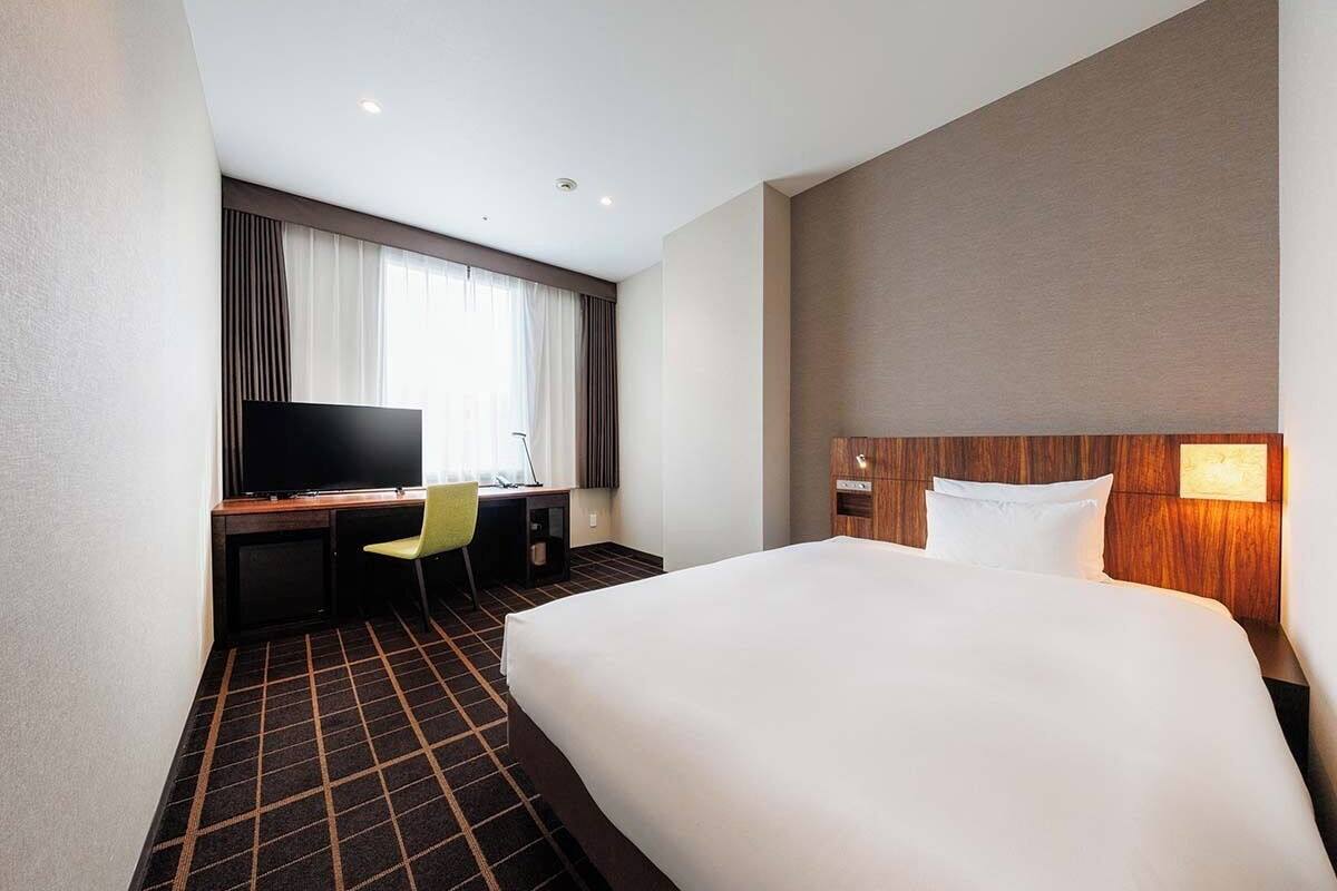 Een hotelkamer met een groot bed, een bureau met stoel, een televisie en een raam met gordijnen.