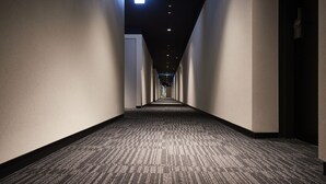 A long, narrow hallway with carpeted floors and walls, leading to a door at the end.