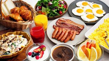 A breakfast spread with croissants, sausages, eggs, and various fruits and beverages.