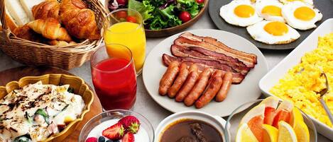 A breakfast spread with croissants, sausages, eggs, and various fruits and beverages.