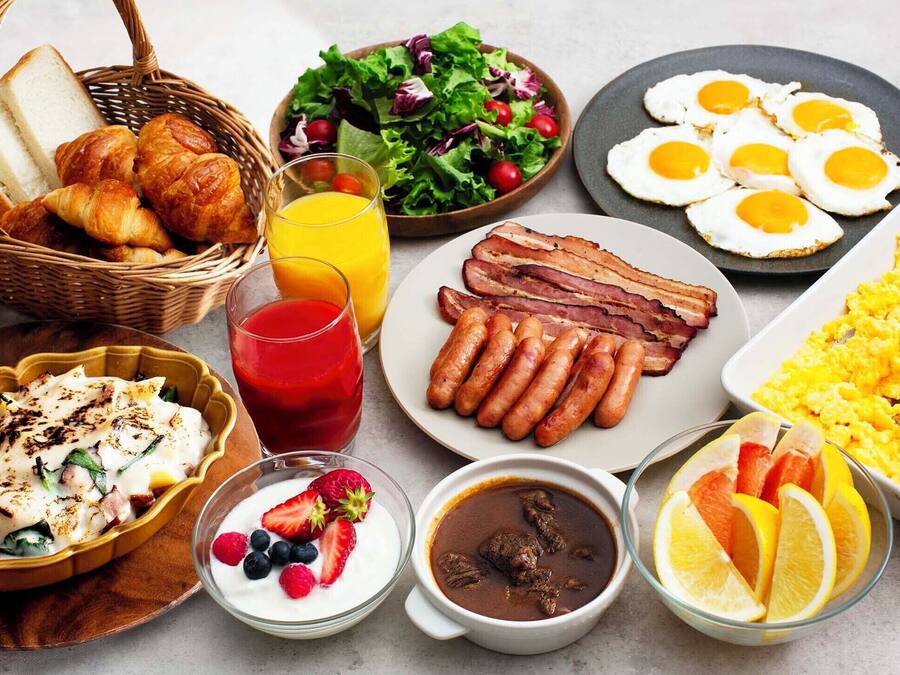 A breakfast spread with croissants, sausages, eggs, and various fruits and beverages.